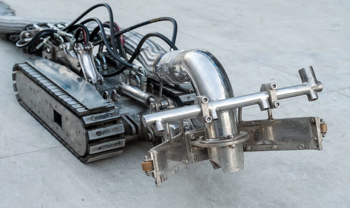 Close-up of an Arham Oil tracked tank-cleaning robot with its suction head and hydraulic hoses.